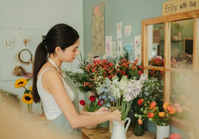 Side view of serious female florist arranging fresh flowers in vase while working in florist studio